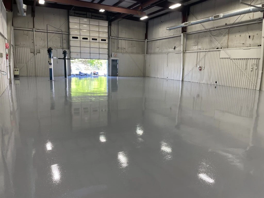 The image displays an industrial epoxy or polyurea floor coating installed in a warehouse or garage setting.