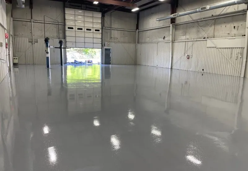 The image displays an industrial epoxy or polyurea floor coating installed in a warehouse or garage setting.